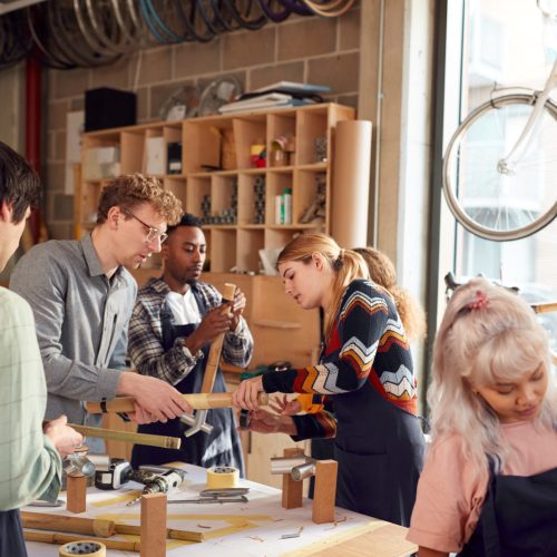 Multi-Cultural Team In Workshop Assembling Hand Built Sustainable Bamboo Bicycle Frame